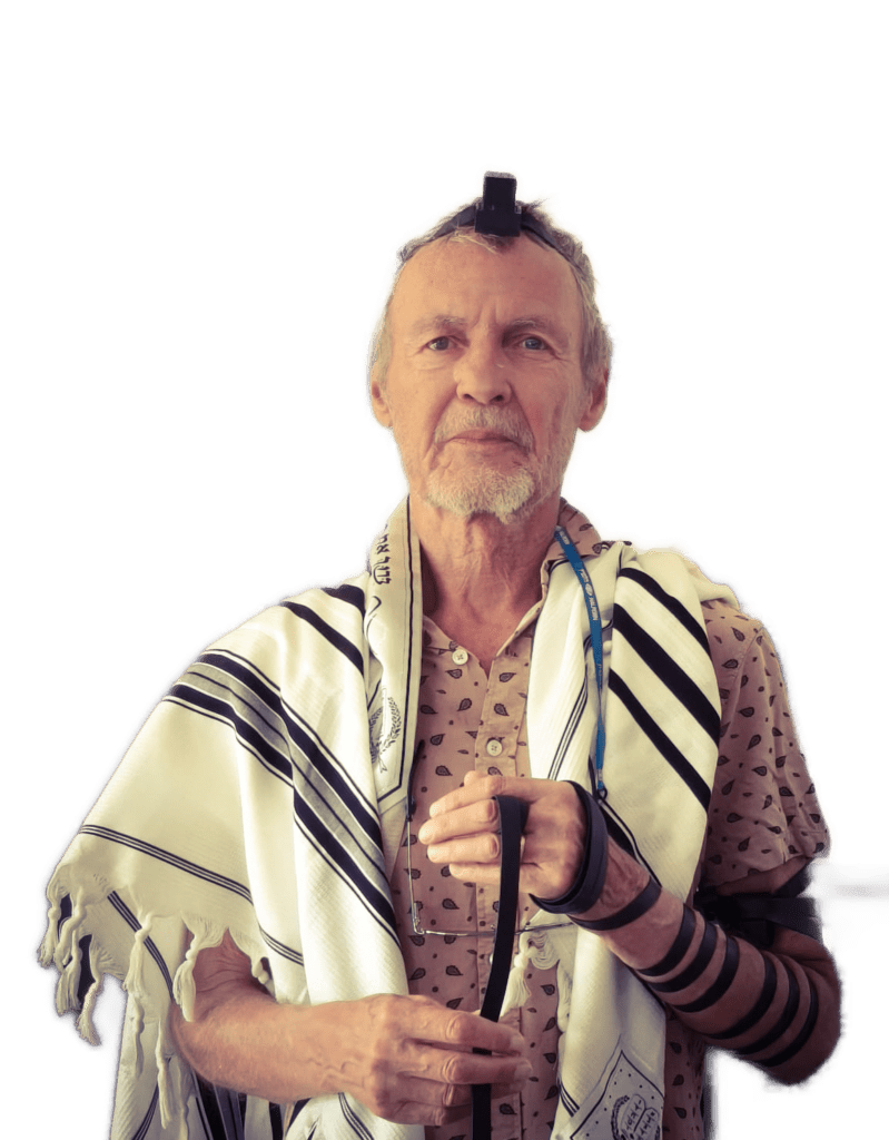 Older man wearing a prayer shawl (tallit) and tefillin, holding a cane during prayer.
