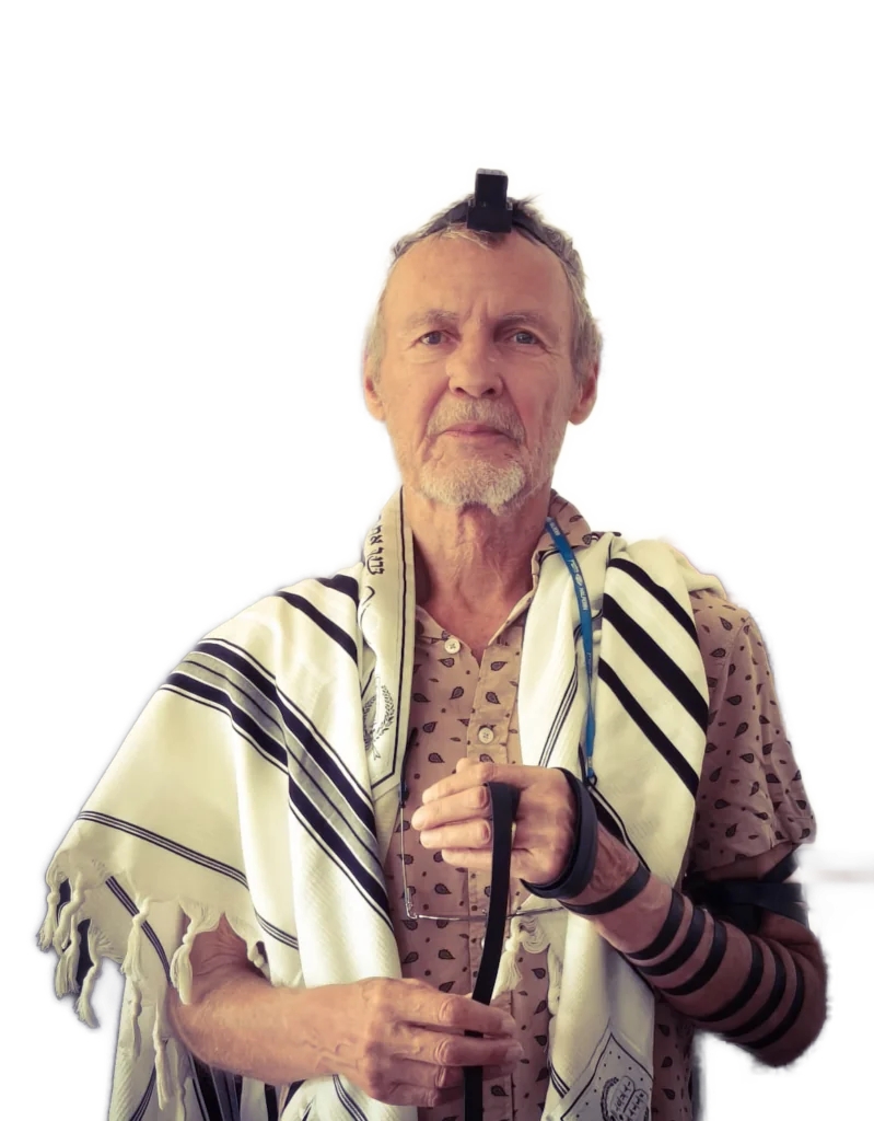 Older man wearing a prayer shawl (tallit) and tefillin, holding a cane during prayer.