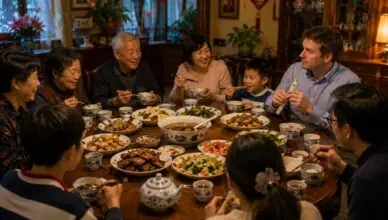 A multiGenerational family sharing a Chinese festive dinner around a round table with assorted dishes and tea cups.